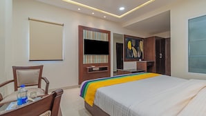 A hotel room with a bed, a desk with a chair, a TV, and a wardrobe. - Itsy Hotels P Grand (Ludhiana)