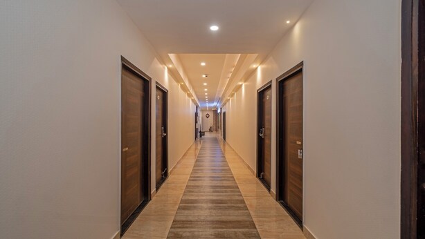 A hotel hallway with wooden doors, a carpeted floor, and recessed lighting. - Itsy Hotels P Grand (Ludhiana)