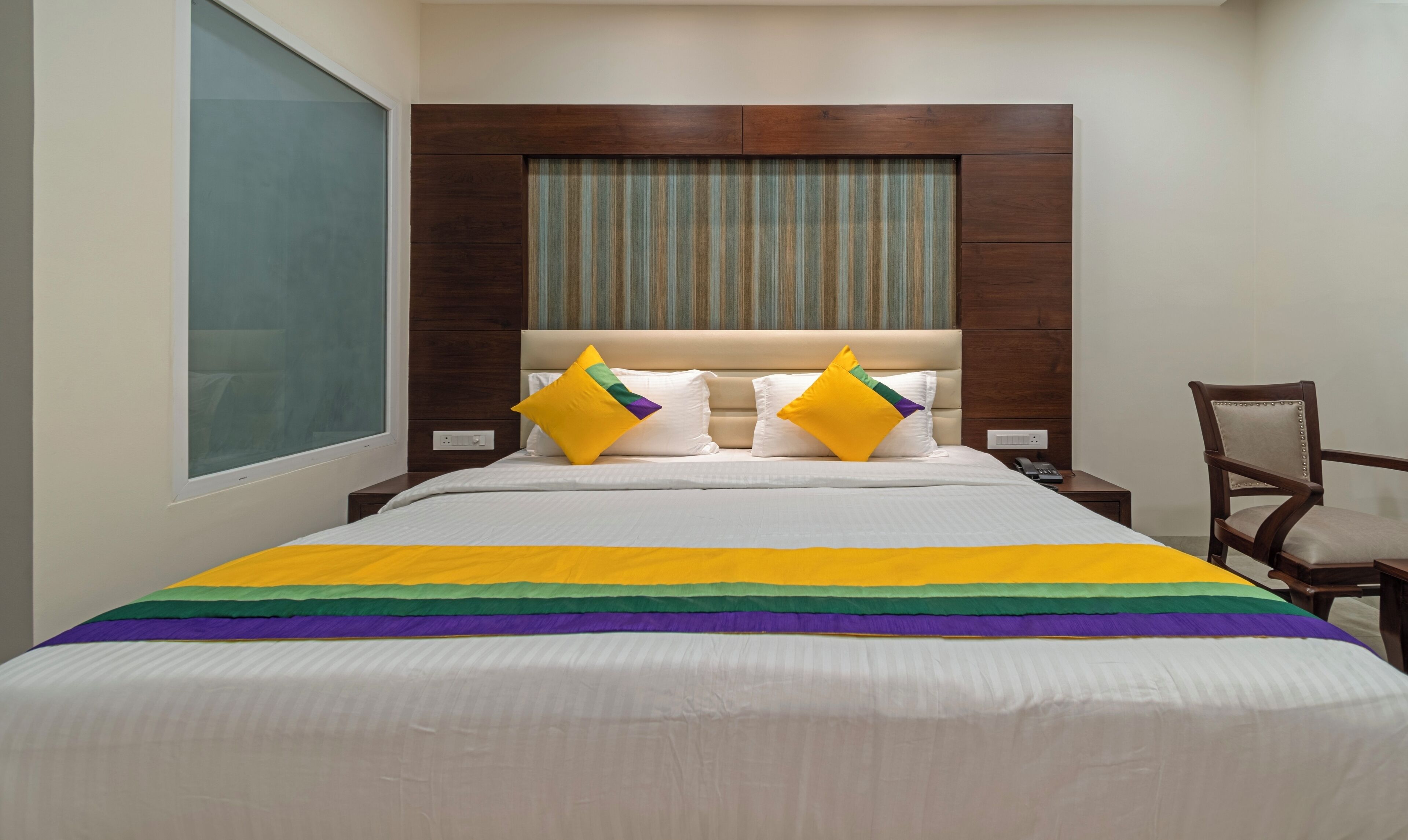 A hotel room with a large bed, a wooden headboard, a nightstand with a phone, and a chair.