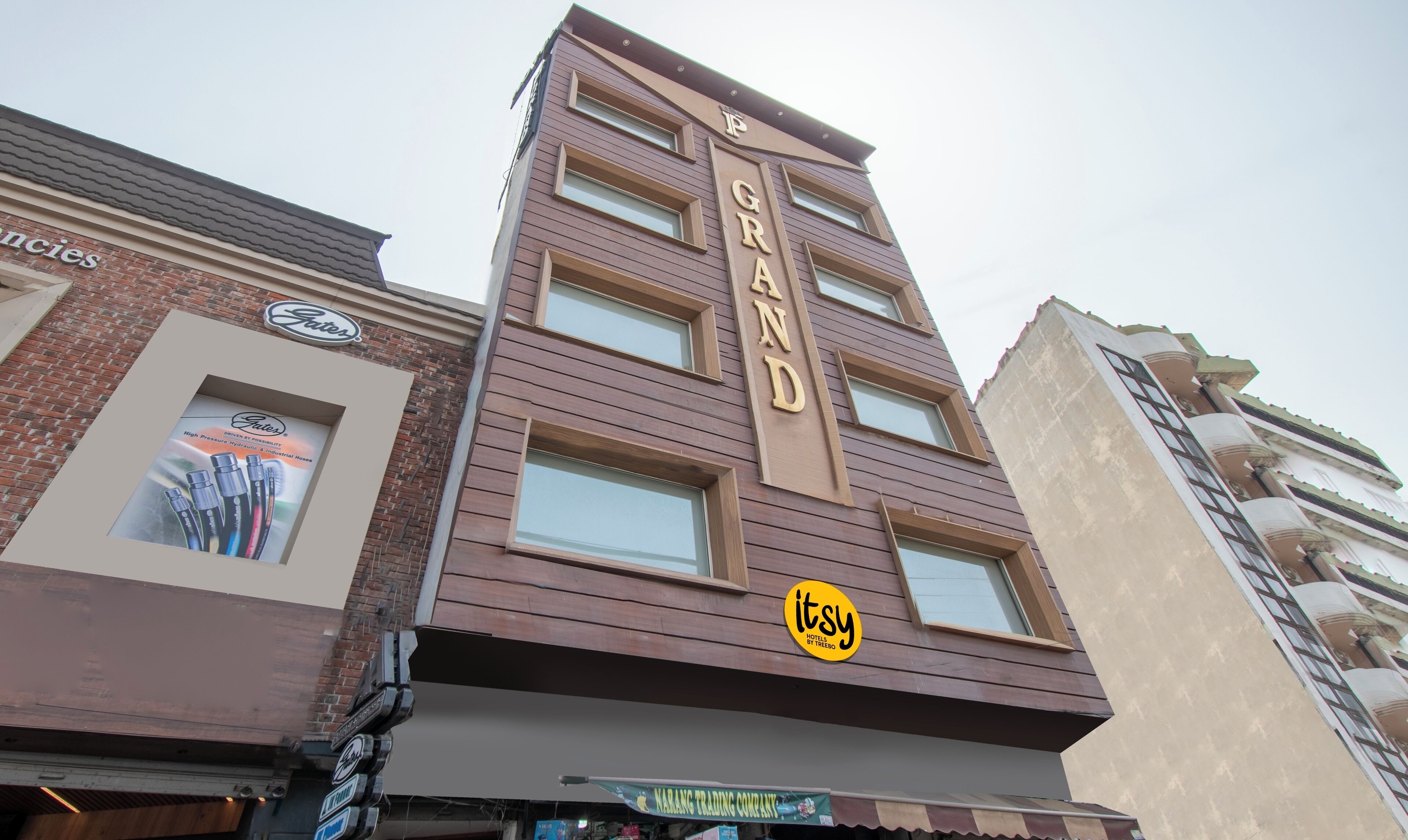 Un hotel llamado 'Grand' con una fachada moderna, múltiples ventanas y un letrero que dice 'Marang Trading Company' debajo.