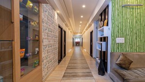 A hallway with a wooden floor, a green wall with vertical bamboo patterns, and a sofa with a cushion. - Itsy Hotels P Grand (Ludhiana)