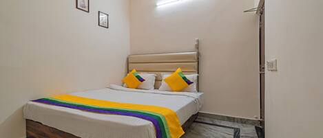 A bedroom with a bed, a headboard, a bedside table, a nightstand, a wall-mounted light, and a door.