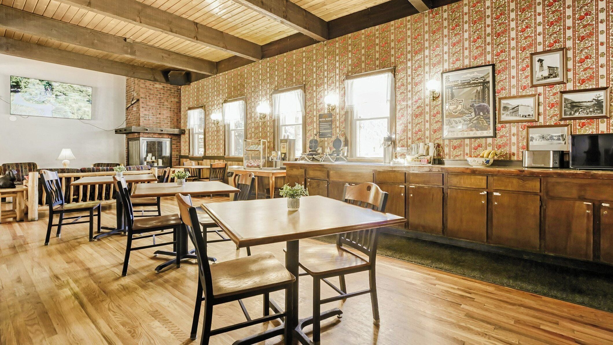 A restaurant with wooden tables and chairs, a brick wall, and a kitchen area.