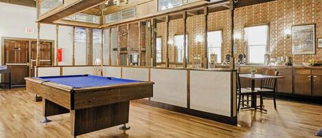 A pool table in a room with wooden floors and a high ceiling.