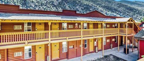 Et flere etagers hotel i træ med balkoner, en overdækket veranda og et bjergrigt baggrundsmotiv.