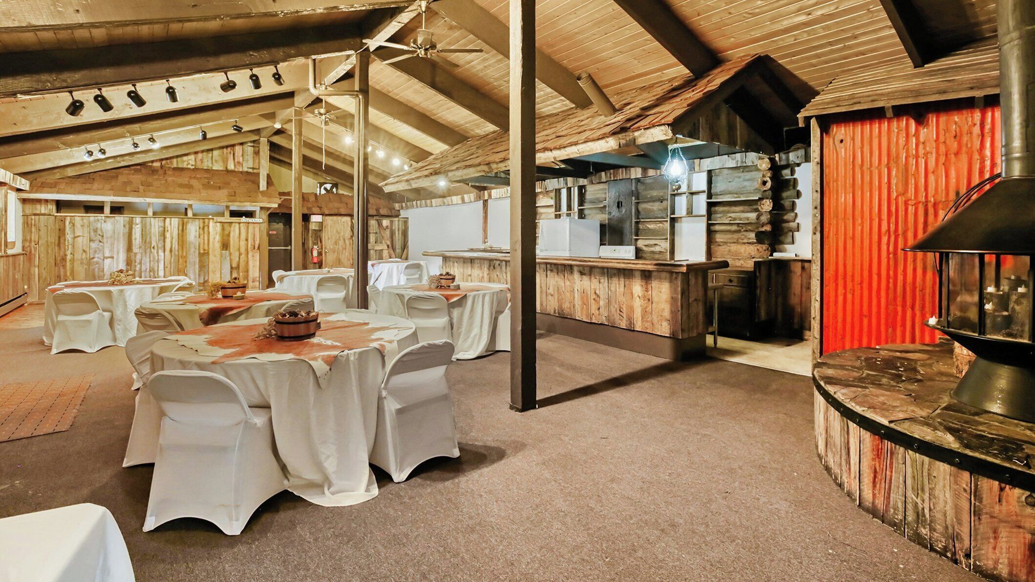 A rustic dining area with round tables, white tablecloths, and a red wall.