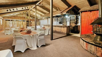 Un coin repas au décor rustique, avec des tables rondes, des nappes blanches et un mur rouge.