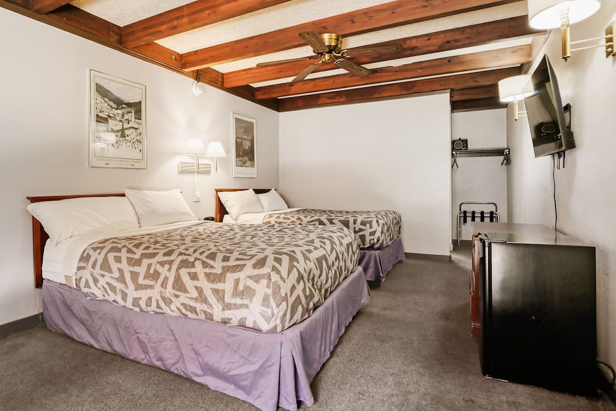 A bedroom with two beds, a ceiling fan, wall-mounted lights, a refrigerator, and framed pictures on the wall.