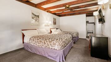 A bedroom with two beds, a ceiling fan, wall-mounted lights, a refrigerator, and framed pictures on the wall.