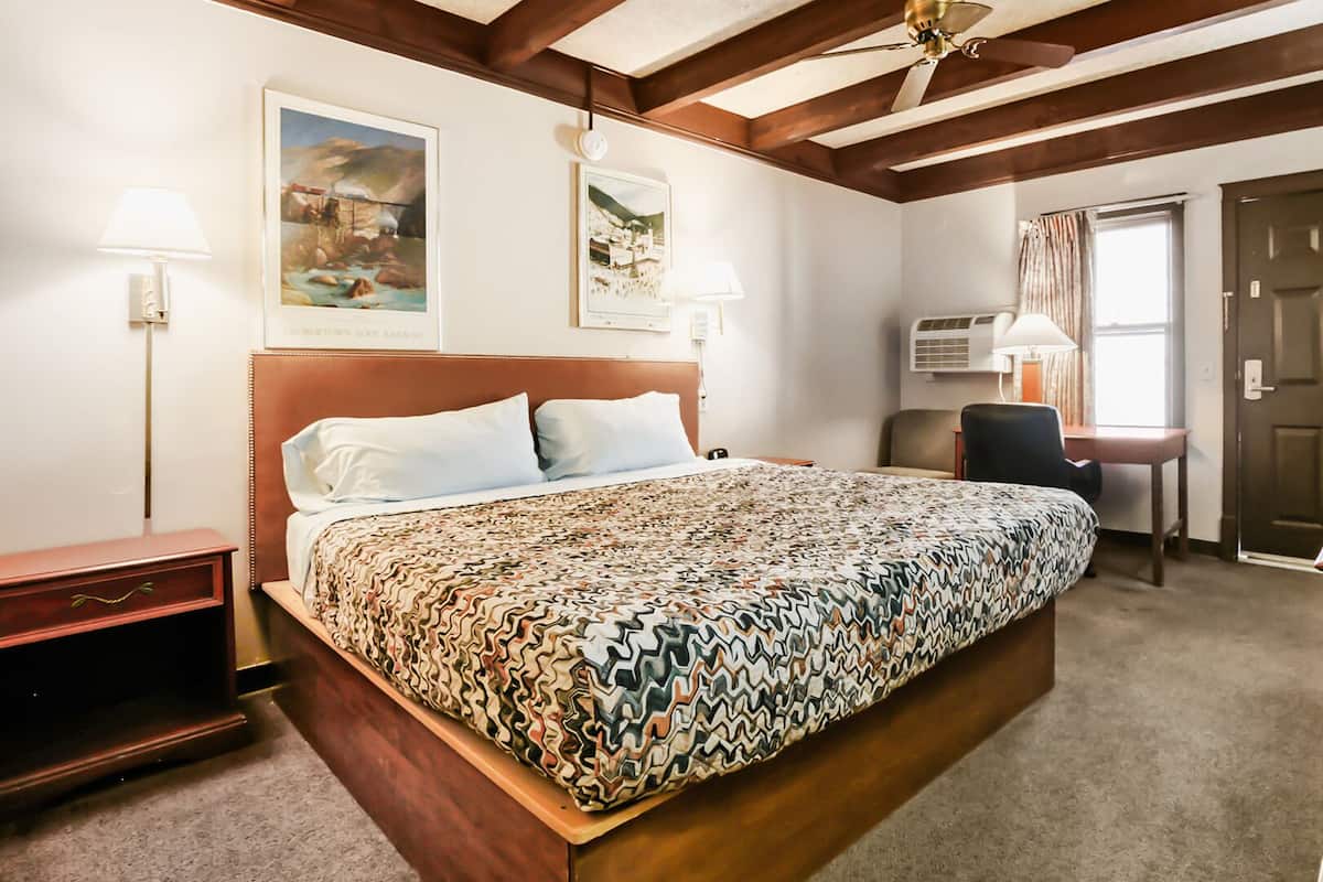 A hotel room with a large bed, a desk, a chair, a wardrobe, and a door.