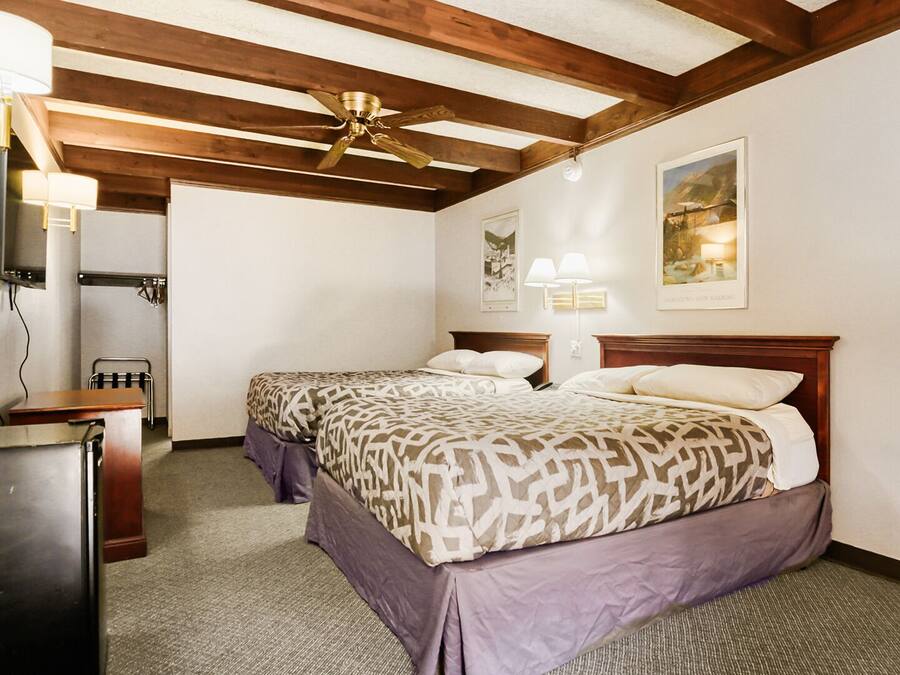 A hotel room with two beds, a desk, a ceiling fan, and artwork on the walls.