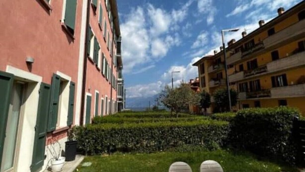 A courtyard with a table and chairs, surrounded by buildings with balconies and a clear sky. - DV Garda Suite 55.0 (Campione del garda)