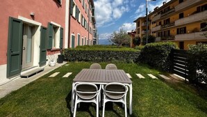 A courtyard with a table and chairs, surrounded by buildings with balconies and a hedge. - DV Garda Suite 55.0 (Campione del garda)