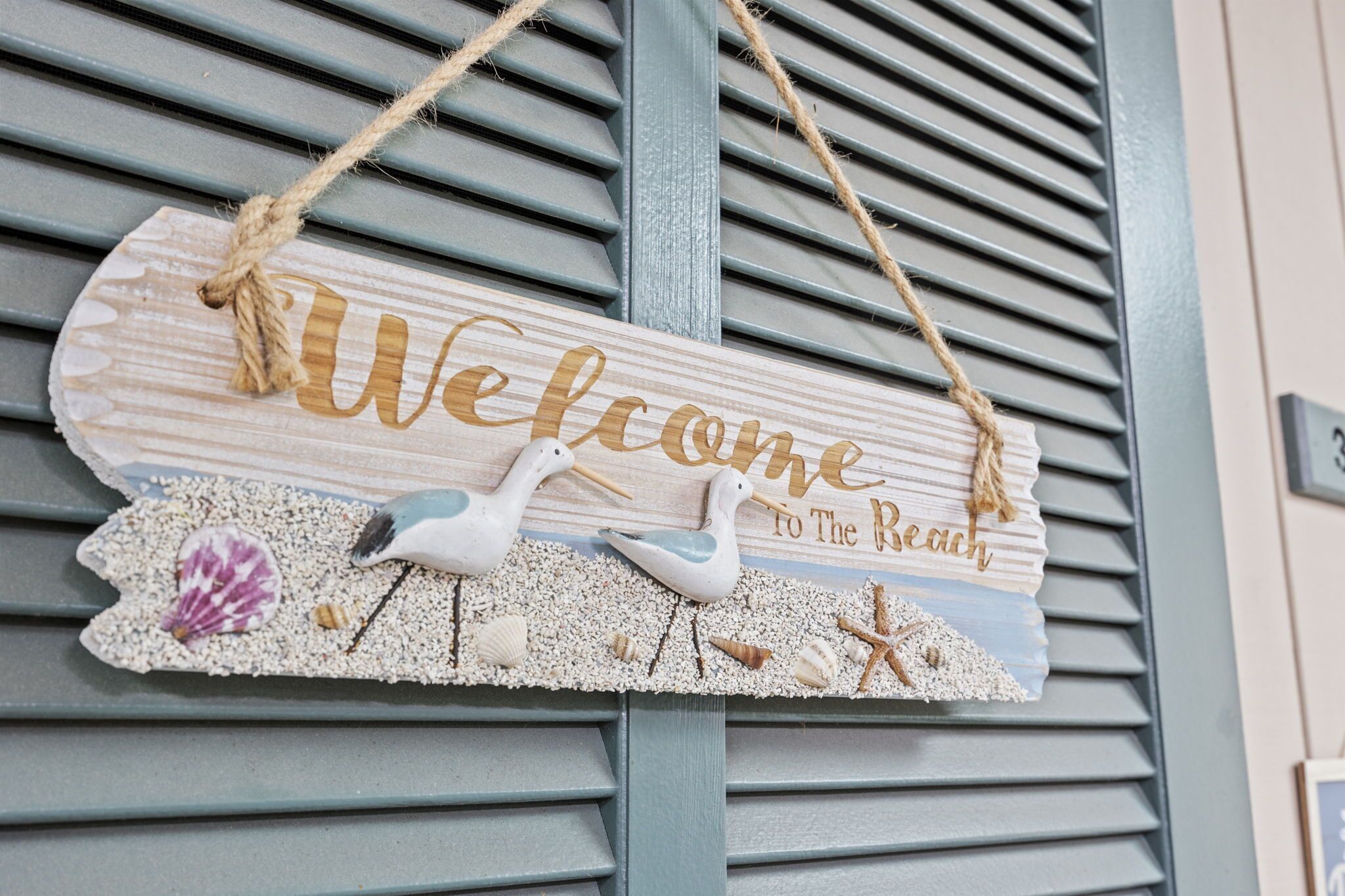 Un cartell de fusta amb la inscripció 'Welcome to The Beach' i elements decoratius com closques i gaviotxes.