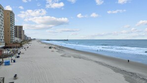 En bred strand med en moler, der strækker sig ud i havet, omgivet af høje bygninger.