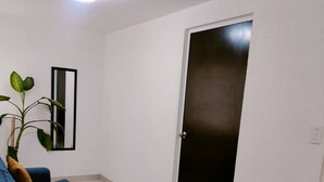 A living room with a blue sofa, a potted plant, and a door. - Autódromo Apartment, Foro Solo, Cdmx Airport (Ciudad de México)
