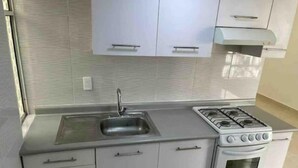 A compact kitchen with a sink, stove, and white cabinets. - Autódromo Apartment, Foro Solo, Cdmx Airport (Ciudad de México)