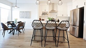 Une cuisine moderne avec des meubles blancs, un réfrigérateur en acier inoxydable et un coin repas comprenant une table ronde et quatre tabourets de bar.