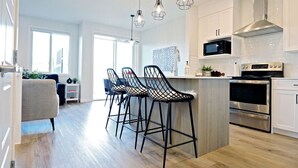 Une cuisine moderne dotée d’un îlot central, de tabourets de bar, d’appareils électroménagers en acier inoxydable et de luminaires suspendus.