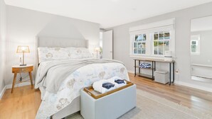 Une chambre à coucher comprenant un lit, des lampes de chevet, une petite table, une fenêtre et une table de chevet avec une lampe.
