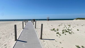 Un sentier bordant la plage, menant à l’océan, avec un poste de surveillance des sauveteurs visible au loin.