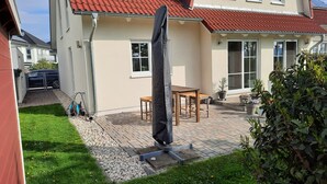 Ein Haus mit rotem Ziegeldach, Solaranlage, gepflasterter Terrasse und kleinem Garten.