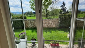Blick durch eine Glastür auf einen Garten mit einer Steinmauer, Kübelpflanzen und einer gepflasterten Terrasse.