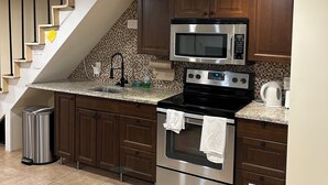A kitchen with a stainless steel stove, microwave, and oven, wooden cabinets, a granite countertop, and a tiled backsplash. - Entire basement apartment - 2067 Park Road, Nw Dc. (Washington)