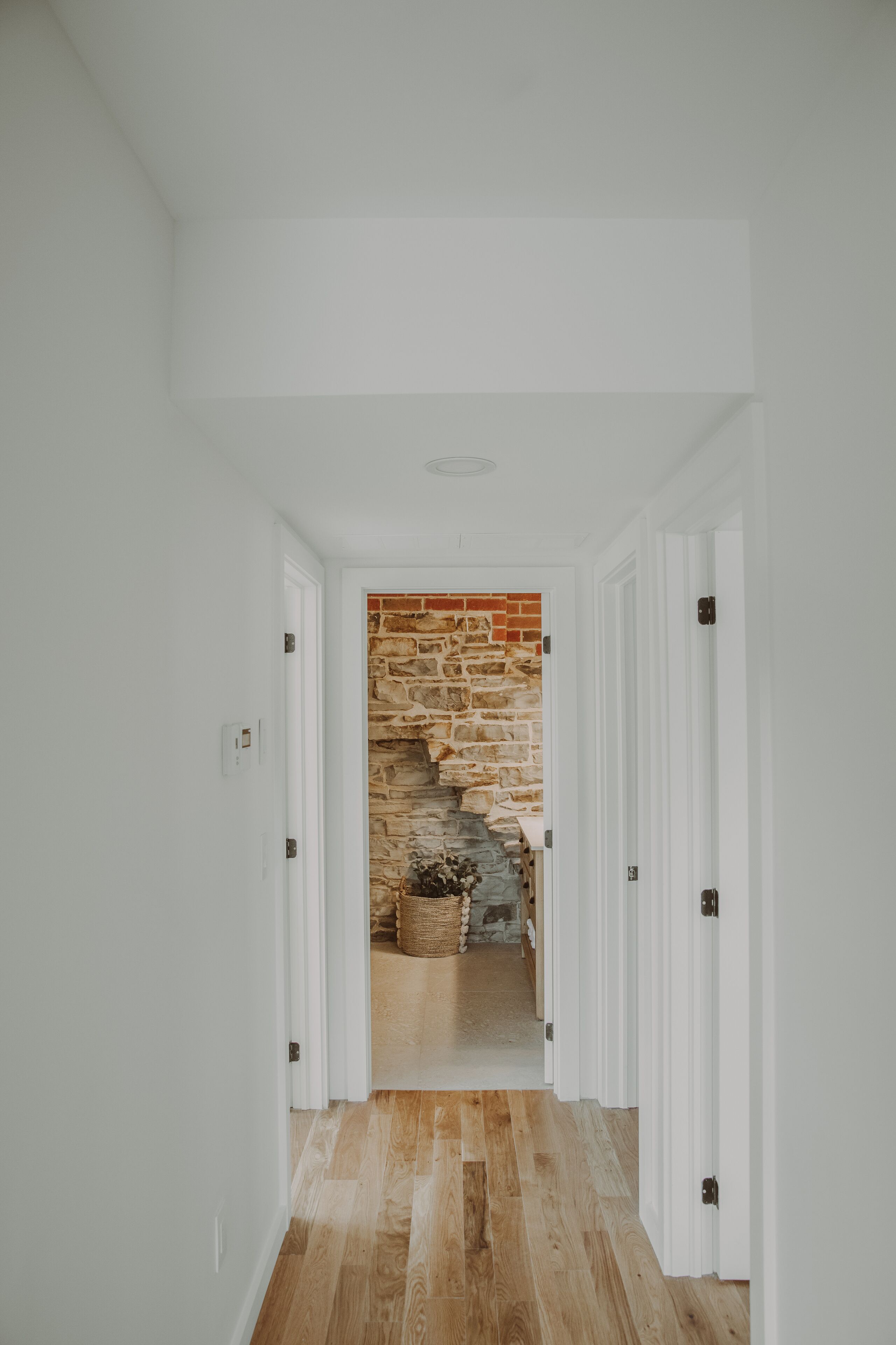A hallway with white walls and wooden flooring leading to a staircase with a stone wall.
