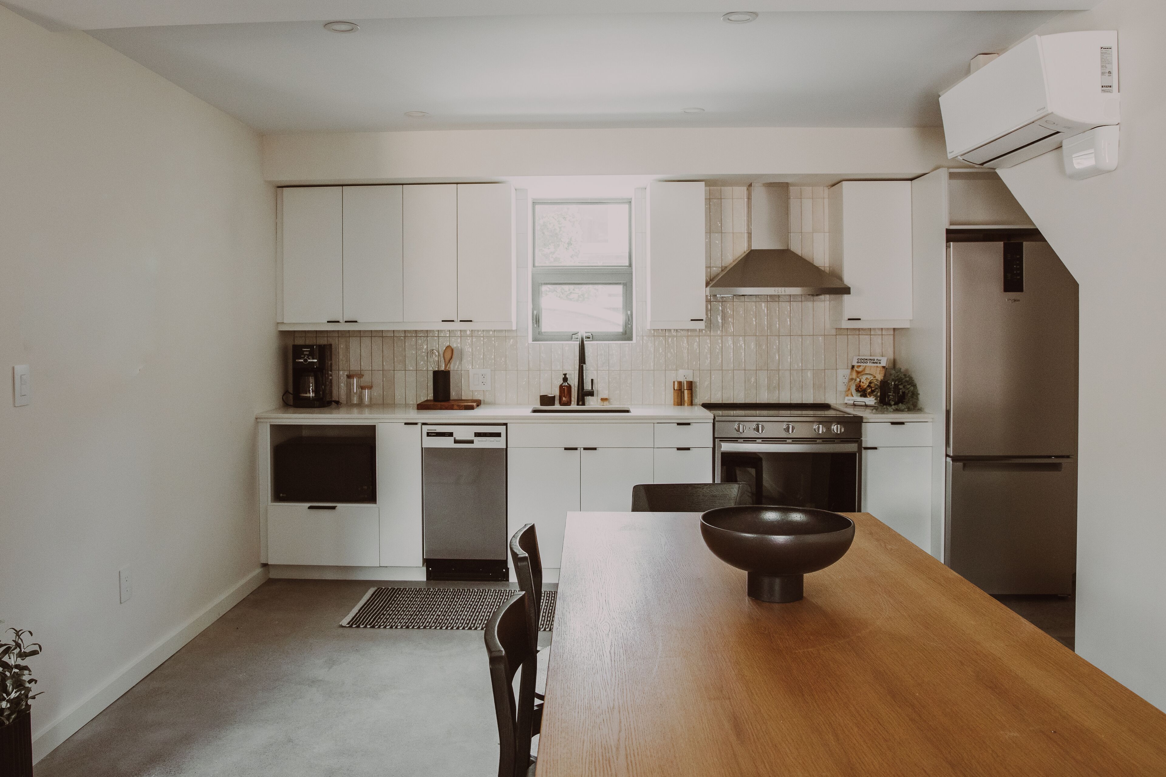 Una cocina moderna con armarios blancos, una mesa de comedor de madera y electrodomésticos de acero inoxidable.