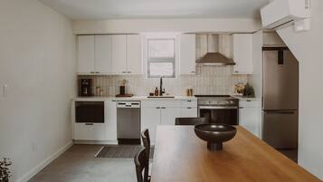 Una cocina moderna con armarios blancos, una mesa de comedor de madera y electrodomésticos de acero inoxidable.