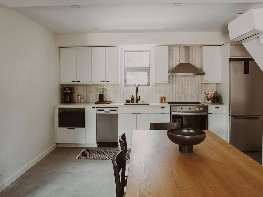 Una cocina moderna con armarios blancos, una mesa de comedor de madera y electrodomésticos de acero inoxidable.