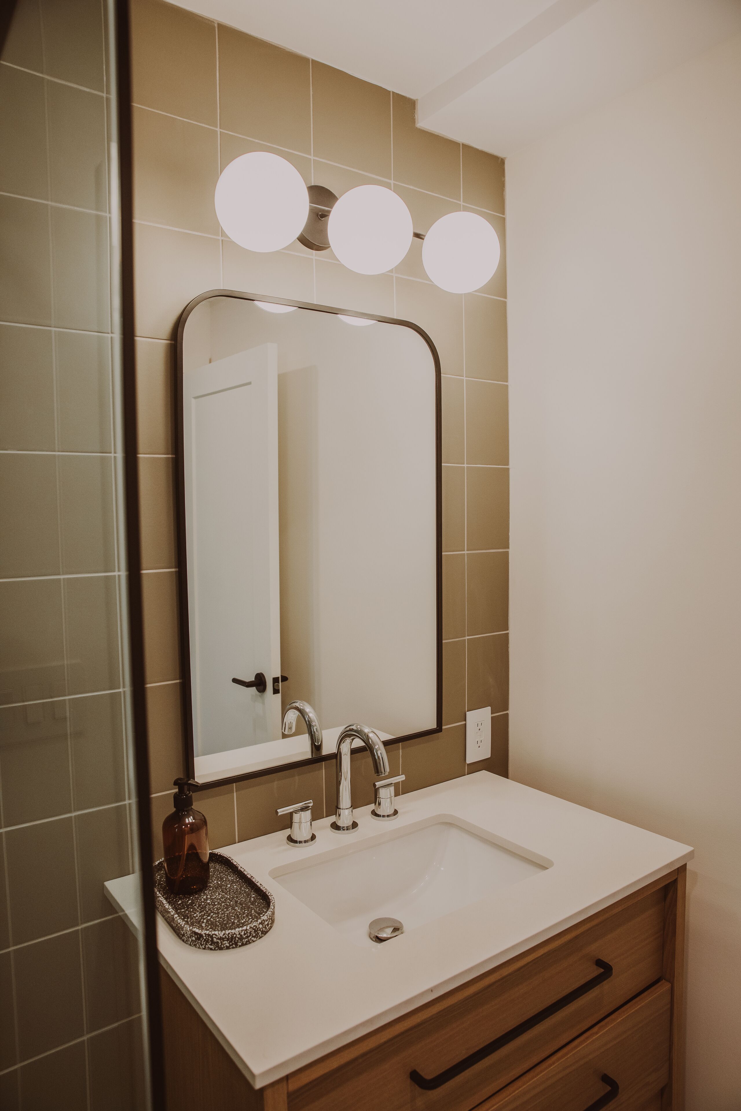 Une salle de bain avec un lavabo blanc, un miroir avec trois lampes et un meuble en bois en dessous.