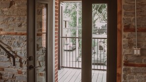 Une pièce avec un mur en pierre, une porte en bois et une vue sur un balcon doté d’une balustrade.