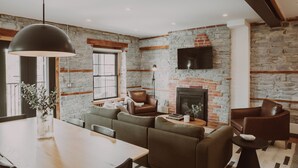 Un salon moderne avec un mur en pierre, une cheminée, des canapés en cuir et un coin repas doté d’une table en bois.