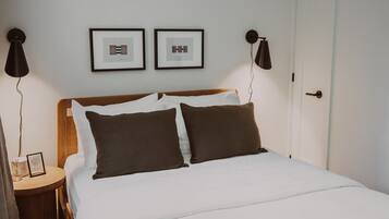 A neatly made bed with white and brown bedding, two framed pictures on the wall, and a bedside table with a lamp.