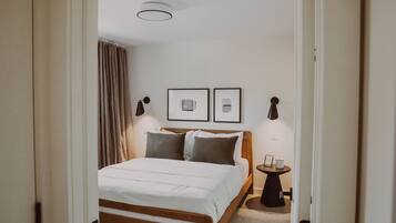 Un dormitorio con una cama de madera, dos lámparas de noche, una mesita con una vela y dos cuadros en la pared.
