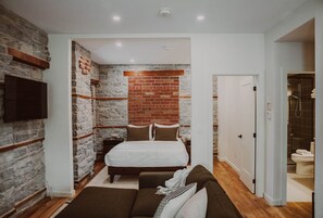 Un dormitorio con pared de ladrillo, una cama, televisor y zona de ducha.