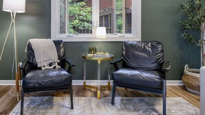 A room with two black leather chairs, a small round table with a lamp, and a view of a wooden deck through a window. - Spacious townhome within steps of Apple Valley Golf Course--Indoor pool! (lake lure)