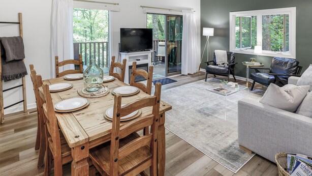 A spacious living room with a wooden dining table set for six, a grey sofa, and a TV on a stand. - Spacious townhome within steps of Apple Valley Golf Course--Indoor pool! (lake lure)