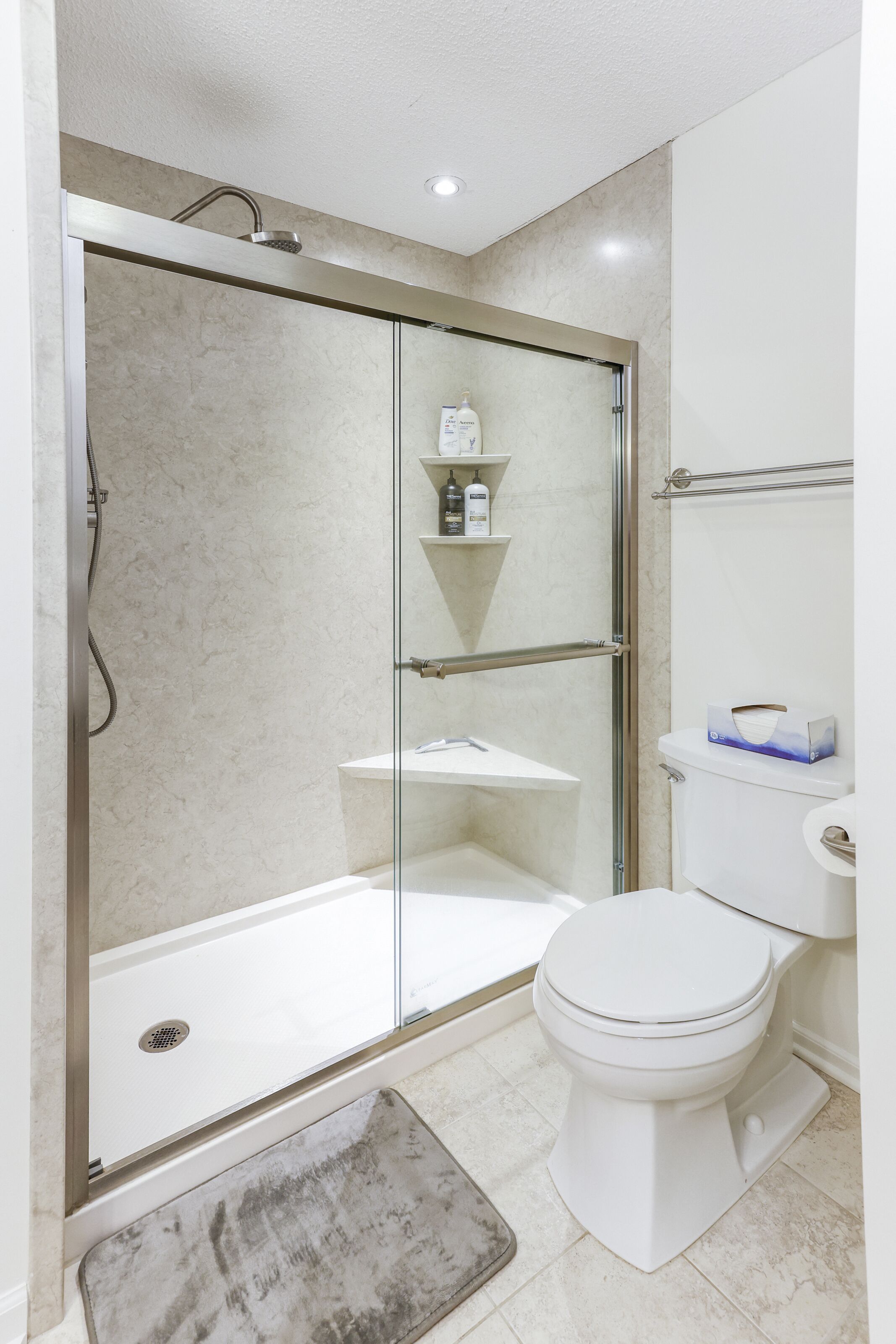 Ein Badezimmer mit einer Duschkabine, einer weißen Toilette und einem kleinen Ablagebereich für Pflegeprodukte.