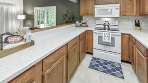 A kitchen with wooden cabinets, a white countertop, a microwave, an oven, and a tiled backsplash. - Spacious townhome within steps of Apple Valley Golf Course--Indoor pool! (lake lure)