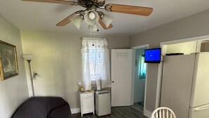 A compact living space with a ceiling fan, a dining table, a sofa, a small refrigerator, and a television. - Quiet Cottage in the heart of Burr Oak State Park. (Glouster)