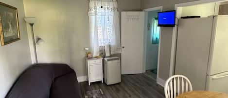 A compact living space with a ceiling fan, a dining table, a sofa, a small refrigerator, and a television.