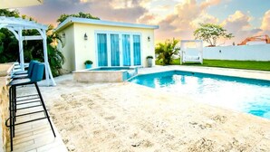 A modern pool area with a clear blue pool, a covered seating area, and a small building with large windows. - Tropical Retreat Stay-Spacious 5BR Oasis with Pool, Solar Backup, for 20 Guests! (caimital alto)