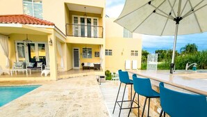 A poolside area with a bar, blue chairs, and a large umbrella. - Tropical Retreat Stay-Spacious 5BR Oasis with Pool, Solar Backup, for 20 Guests! (caimital alto)
