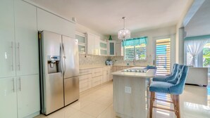 A modern kitchen with stainless steel appliances, a central island with bar stools, and a chandelier. - Tropical Retreat Stay-Spacious 5BR Oasis with Pool, Solar Backup, for 20 Guests! (caimital alto)