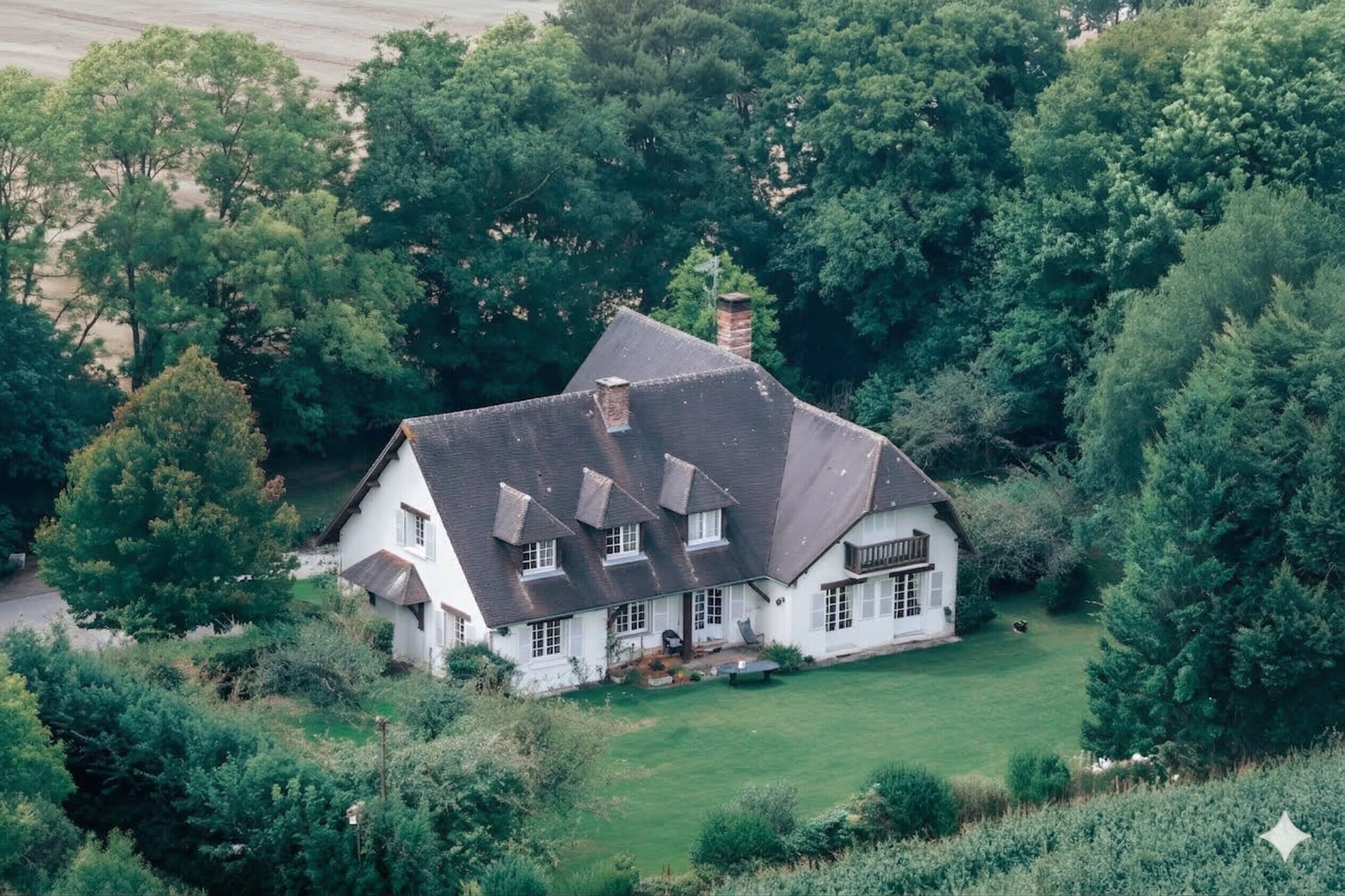 A white house with a steep roof, surrounded by dense greenery and trees.