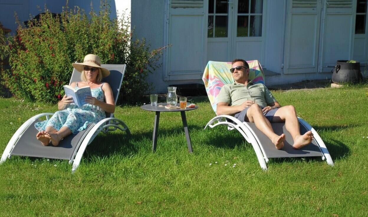 Deux fauteuils inclinables sont placés dans un espace herbeux, avec une petite table entre eux.