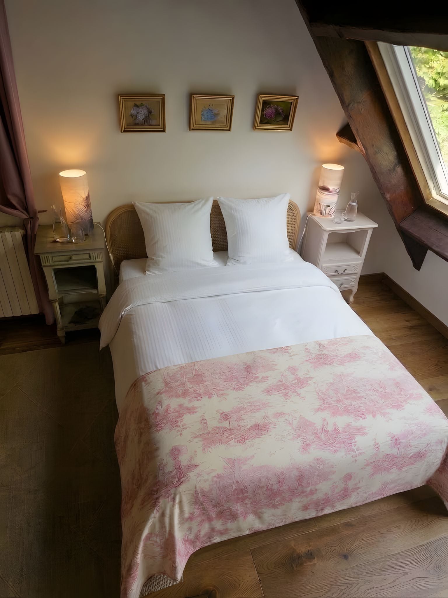 A bedroom with a bed, two bedside tables, a window, and three framed pictures on the wall.